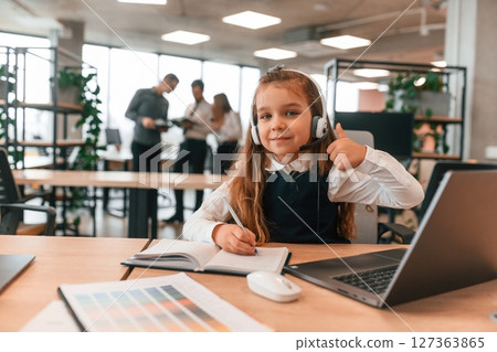 Laptop is on the table. Little girl is in the office where people working together Laptop is on the table. Little girl is in the office where people working together 127363865