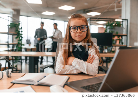 Laptop is on the table. Little girl is in the office where people working together 127363866