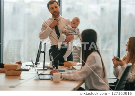 Man with his son. Infant baby is in the office where group of people are working together 127363916