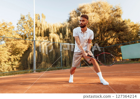 Active training. Young man is on the tennis court at sunny daytime Active training. Young man is on the tennis court at sunny daytime 127364214
