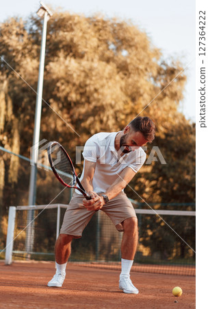 Young man is on the tennis court at sunny daytime Young man is on the tennis court at sunny daytime 127364222