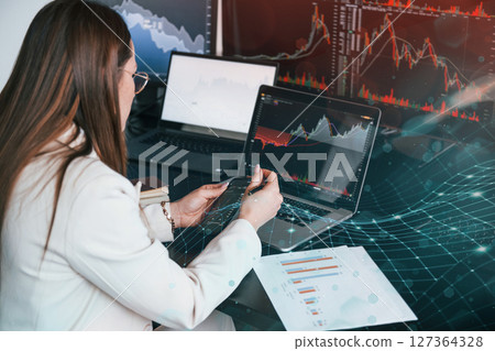Many of the graphs and data. Young female stock brocker works indoors in the office. Many of displays Many of the graphs and data. Young female stock brocker works indoors in the office. Many of displays 127364328