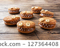 Cookies with cream paste in the shape of monsters for Halloween celebration. Funny homemade faces made of oatmeal cookies and boiled condensed milk. 127364408