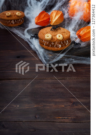 Cookies with cream paste in the shape of monsters for Halloween celebration. Funny homemade faces made of oatmeal cookies and boiled condensed milk. copy space 127364412