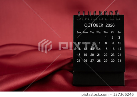 Black desk calendar for October 2026 on a red color satin or silk textile background. 127366246