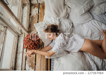 sexy woman in white shirt in bed by the window with a bouquet 127367064