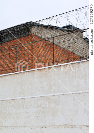High Brick Wall with Barbed Wire Surrounding a Prison: A Symbol of Confinement and Security High Brick Wall with Barbed Wire Surrounding a Prison: A Symbol of Confinement and Security 127369279