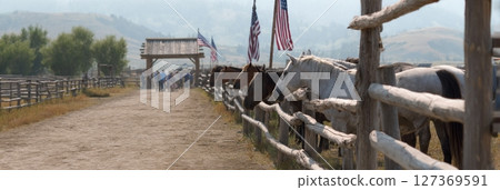 Horses lined up along rustic wooden fence with American flags, showcasing cowboy culture and prairie life 127369591