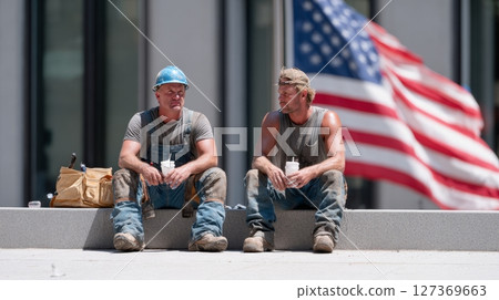 Construction workers relax with drinks in hand, sharing a break under warm sunlight and an American flag 127369663