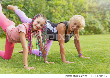 Girl and mature woman are together in yoga cat pose. 127370487