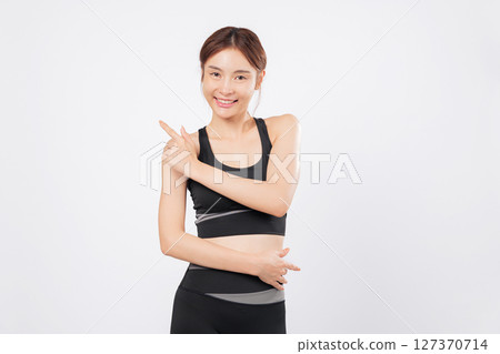 Pointing up with fit presence, this Asian woman shares another point of joy and motivation, wearing sleek sportswear and promoting positive attitude in fitness and sports. isolated white background 127370714