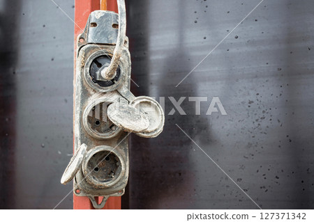 Electrical outlet attached to a wall in a rustic setting showing signs of wear and weathering 127371342