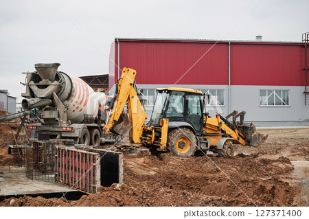 Construction equipment at work on a building site in an industrial area during overcast weather 127371400