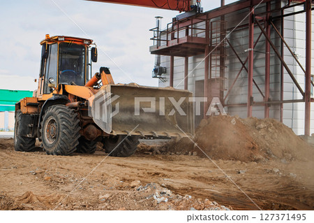 Construction site activity with a heavy machinery loader moving dirt near a building Construction site activity with a heavy machinery loader moving dirt near a building 127371495