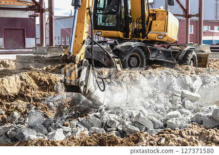 Professional demolition of reinforced concrete structures using industrial hydraulic hammer with excavator. Rods of metal fittings. Wreckage and crumbles of concrete. 127371580