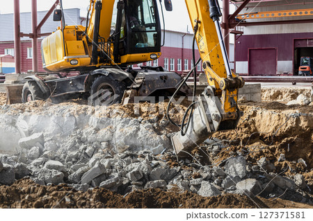 Professional demolition of reinforced concrete structures using industrial hydraulic hammer with excavator. Rods of metal fittings. Wreckage and crumbles of concrete. 127371581