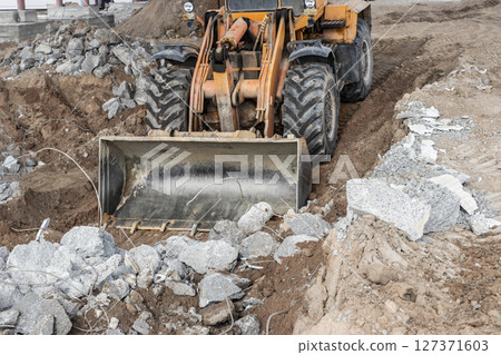 A front-end loader at a construction site removes debris from reinforced concrete. Collection and removal of detached building materials. 127371603