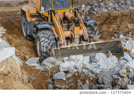 A powerful front loader on a construction site clears up the battle after dismantling reinforced concrete structures. Moving soil with construction equipment. Excavations. A powerful front loader on a construction site clears up the battle after dismantling reinforced concrete structures. Moving soil with construction equipment. Excavations. 127371604