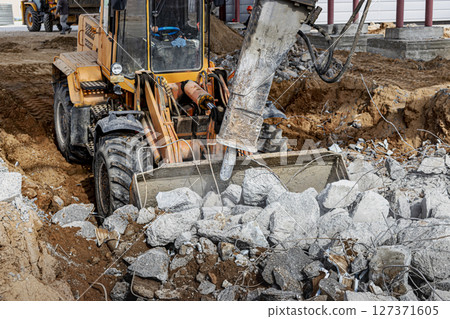 A powerful front loader on a construction site clears up the battle after dismantling reinforced concrete structures. Moving soil with construction equipment. Excavations. A powerful front loader on a construction site clears up the battle after dismantling reinforced concrete structures. Moving soil with construction equipment. Excavations. 127371605