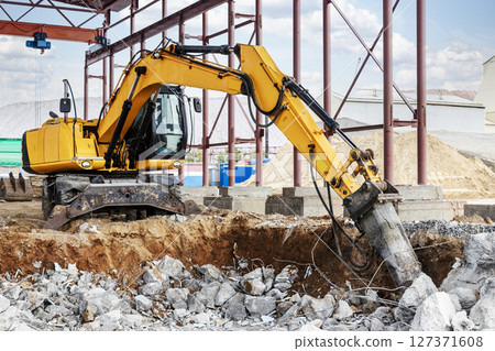 Professional demolition of reinforced concrete structures using industrial hydraulic hammer with excavator. Rods of metal fittings. Wreckage and crumbles of concrete. 127371608
