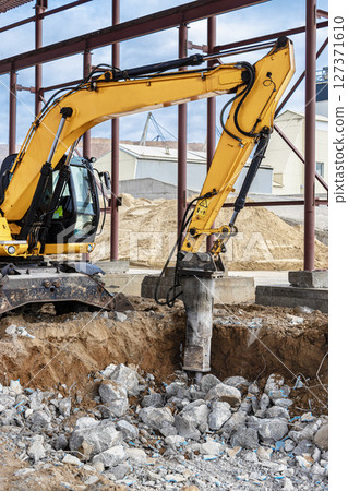 Professional demolition of reinforced concrete structures using industrial hydraulic hammer with excavator. Rods of metal fittings. Wreckage and crumbles of concrete. 127371610