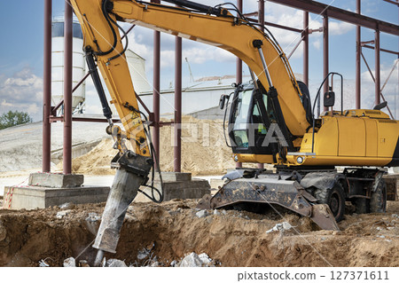 Professional demolition of reinforced concrete structures using industrial hydraulic hammer with excavator. Rods of metal fittings. Wreckage and crumbles of concrete. Professional demolition of reinforced concrete structures using industrial hydraulic hammer with excavator. Rods of metal fittings. Wreckage and crumbles of concrete. 127371611