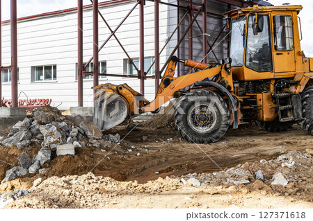A front-end loader at a construction site removes debris from reinforced concrete. Collection and removal of detached building materials. A front-end loader at a construction site removes debris from reinforced concrete. Collection and removal of detached building materials. 127371618