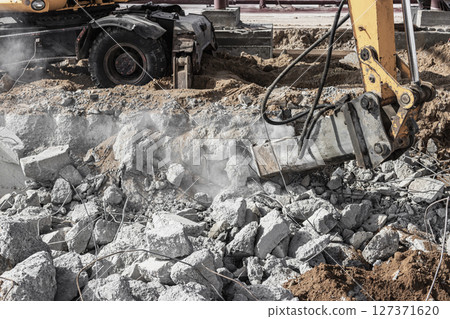 Professional demolition of reinforced concrete structures using industrial hydraulic hammer with excavator. Rods of metal fittings. Wreckage and crumbles of concrete. 127371620