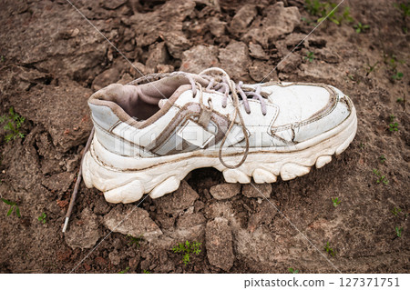 Old sneaker resting on cracked ground in an urban area during daylight hours Old sneaker resting on cracked ground in an urban area during daylight hours 127371751