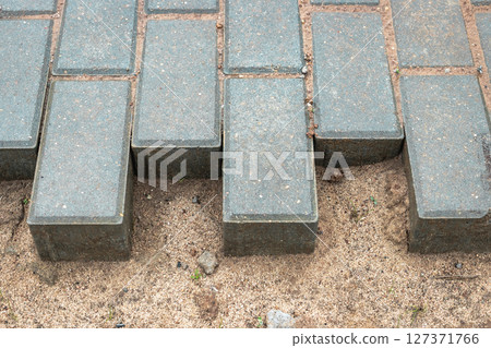Uneven paving stones creating a unique pattern along a sandy path in a garden setting Uneven paving stones creating a unique pattern along a sandy path in a garden setting 127371766