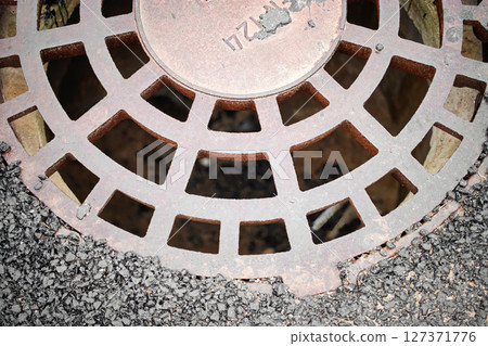 Rusty drain cover resting on asphalt during daylight in an urban environment Rusty drain cover resting on asphalt during daylight in an urban environment 127371776