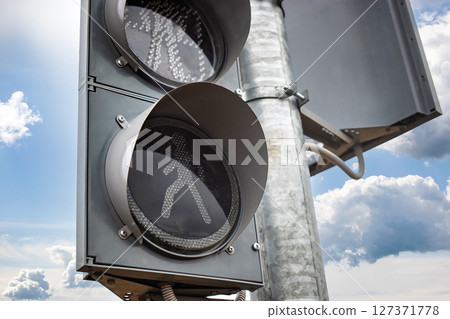 Traffic signal displaying pedestrian walk signal against a cloudy sky 127371778