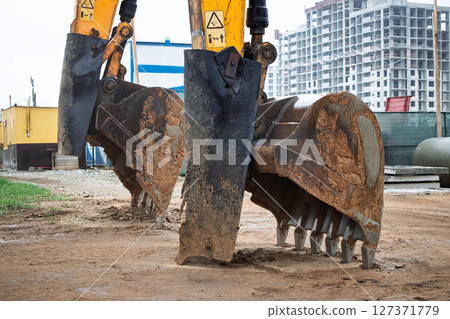Heavy machinery operates on construction site with excavator digging into the ground near a building Heavy machinery operates on construction site with excavator digging into the ground near a building 127371779