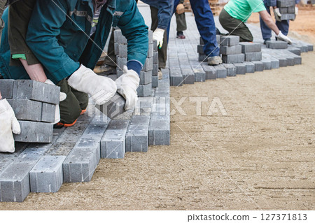 Workers laying grey paving stones during construction at a site in the afternoon light 127371813