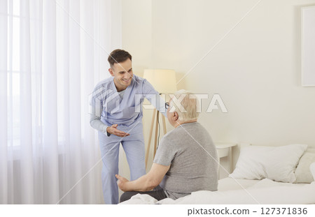 Healthcare professional is attentively engaging with elderly man seated on bed in healthcare room. Healthcare professional is attentively engaging with elderly man seated on bed in healthcare room. 127371836