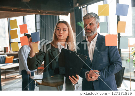 View through the glass full of stickers. Man and woman are standing. Group of business people are working in the modern office 127371859
