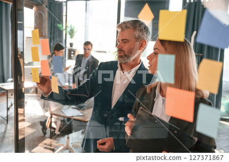 Company growth. Many stickers on the glass. Group of business people are working in the modern office Company growth. Many stickers on the glass. Group of business people are working in the modern office 127371867