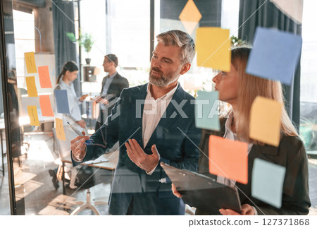 Company growth. Many stickers on the glass. Group of business people are working in the modern office 127371868