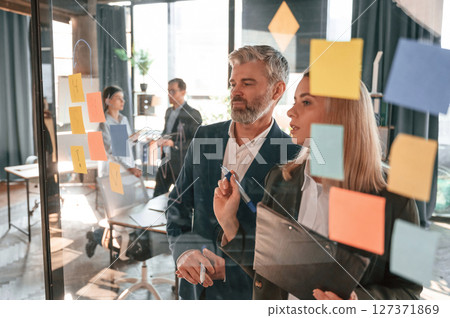 Company growth. Many stickers on the glass. Group of business people are working in the modern office 127371869