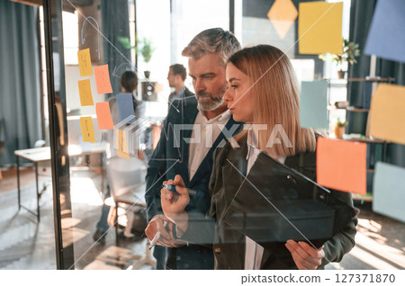 Company growth. Many stickers on the glass. Group of business people are working in the modern office Company growth. Many stickers on the glass. Group of business people are working in the modern office 127371870