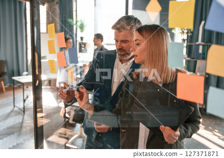 Company growth. Many stickers on the glass. Group of business people are working in the modern office Company growth. Many stickers on the glass. Group of business people are working in the modern office 127371871