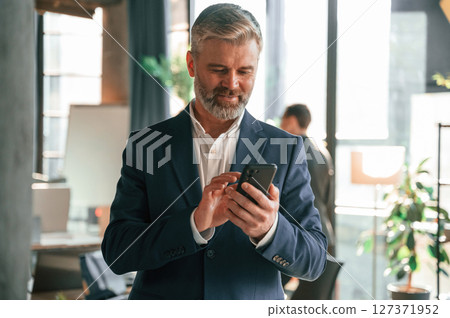Handsome man is standing with smartphone. Business people are working together in the office Handsome man is standing with smartphone. Business people are working together in the office 127371952