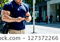 A muscular man walking through the city 127372266