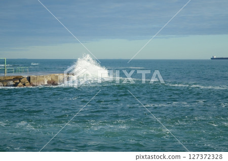 Waves Crashing Against Ocean Seawall with Distant Ship Waves Crashing Against Ocean Seawall with Distant Ship 127372328