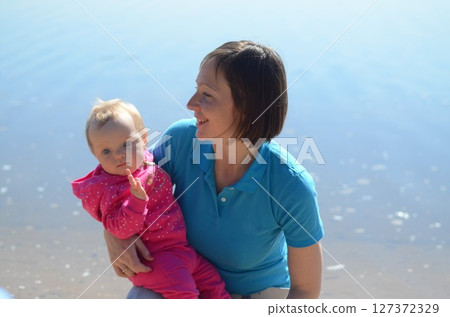 Smiling Mother Holding Baby by the Water's Edge 127372329