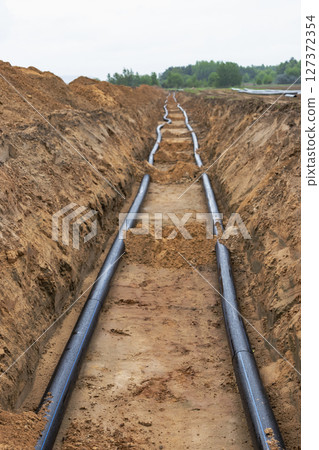 Water pipes for drinking water supply lie on the construction site. Preparation for earthworks for laying an underground pipeline. Modern water supply systems for a residential city. 127372354