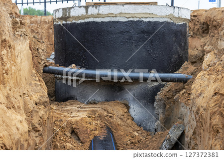Installation of a reinforced concrete well for water supply and sewerage at the construction site. Well rings with cast iron hatch and construction tool. Installation of a reinforced concrete well for water supply and sewerage at the construction site. Well rings with cast iron hatch and construction tool. 127372381