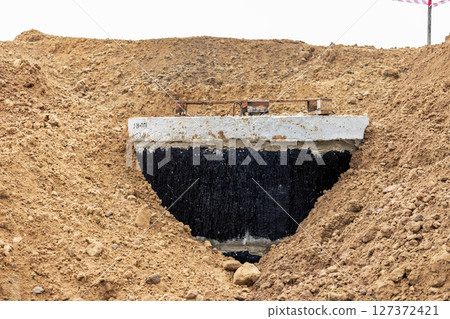 Installation of a reinforced concrete well for water supply and sewerage at the construction site. Well rings with cast iron hatch and construction tool. 127372421
