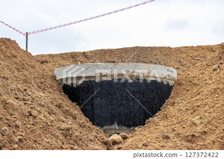 Installation of a reinforced concrete well for water supply and sewerage at the construction site. Well rings with cast iron hatch and construction tool. 127372422