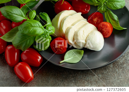 Mozzarella cheese with cherry tomatoes and basil on a stone table. Mozzarella cheese with cherry tomatoes and basil on a stone table. 127372605